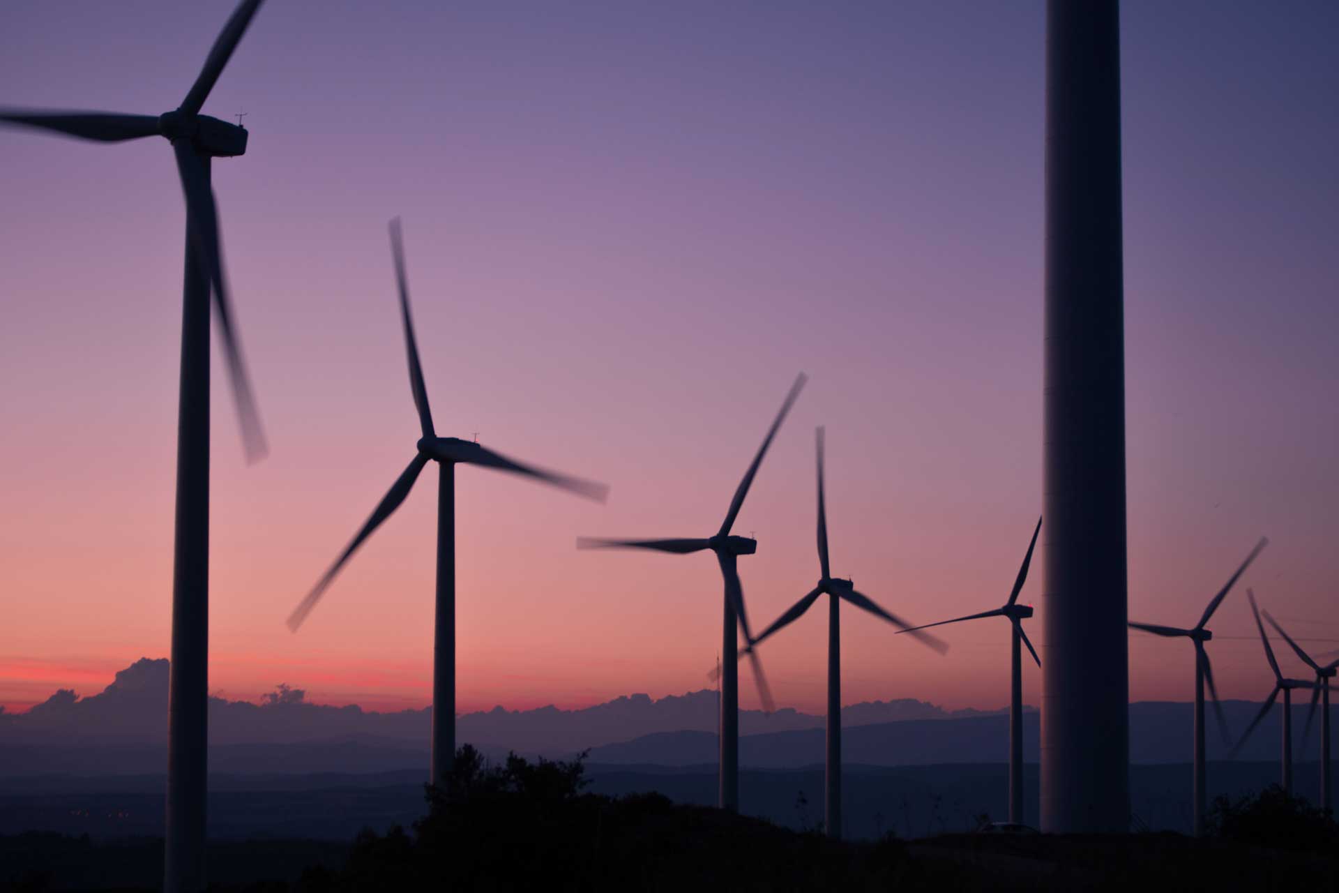 silhouette of windmills spinning at sunset with purple and red sky