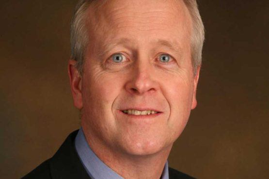 head shot portrait of smiling man with white hair blue eyes shirt and black suit jacket